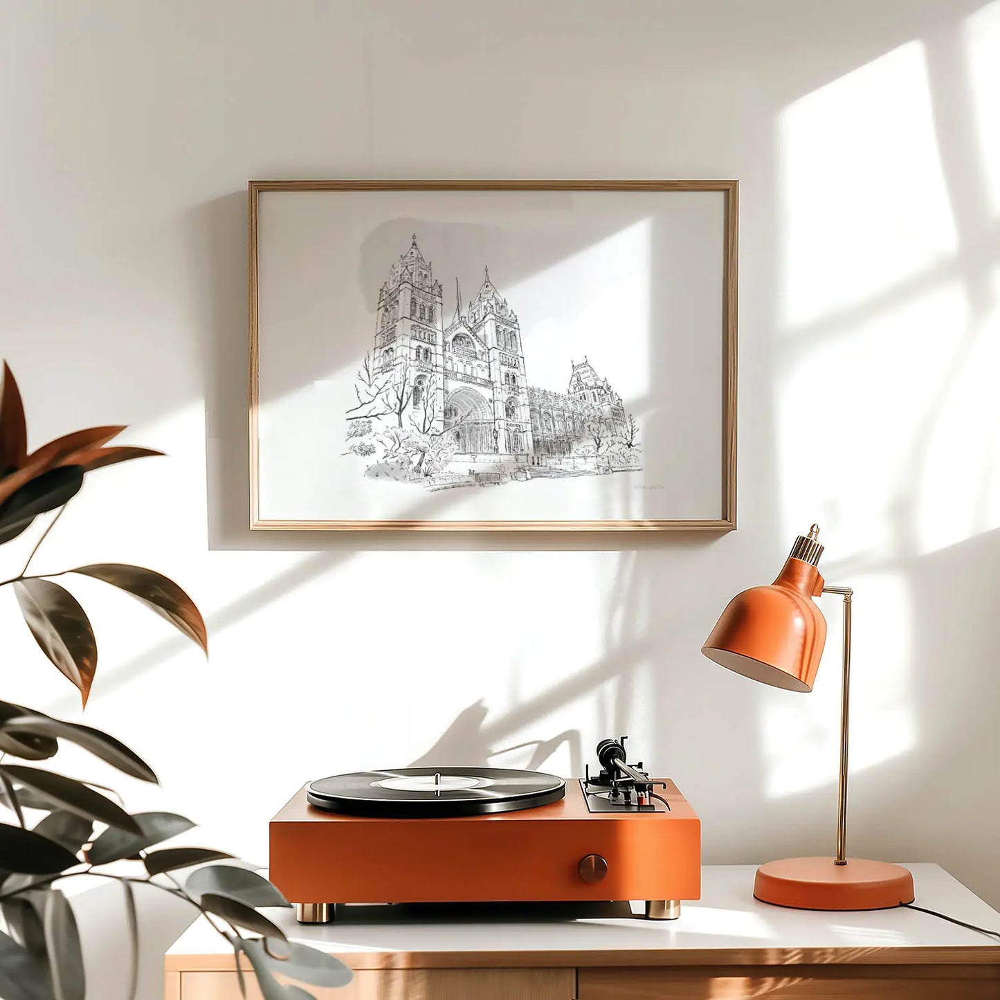 Framed wall art print of a drawing of London's Natural History Museum above a record player and lamp