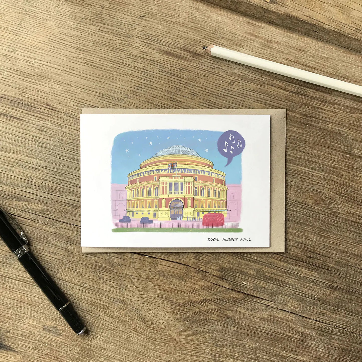 London's Royal Albert Hall illustrated on a greeting card with an envelope and pencil on wooden surface