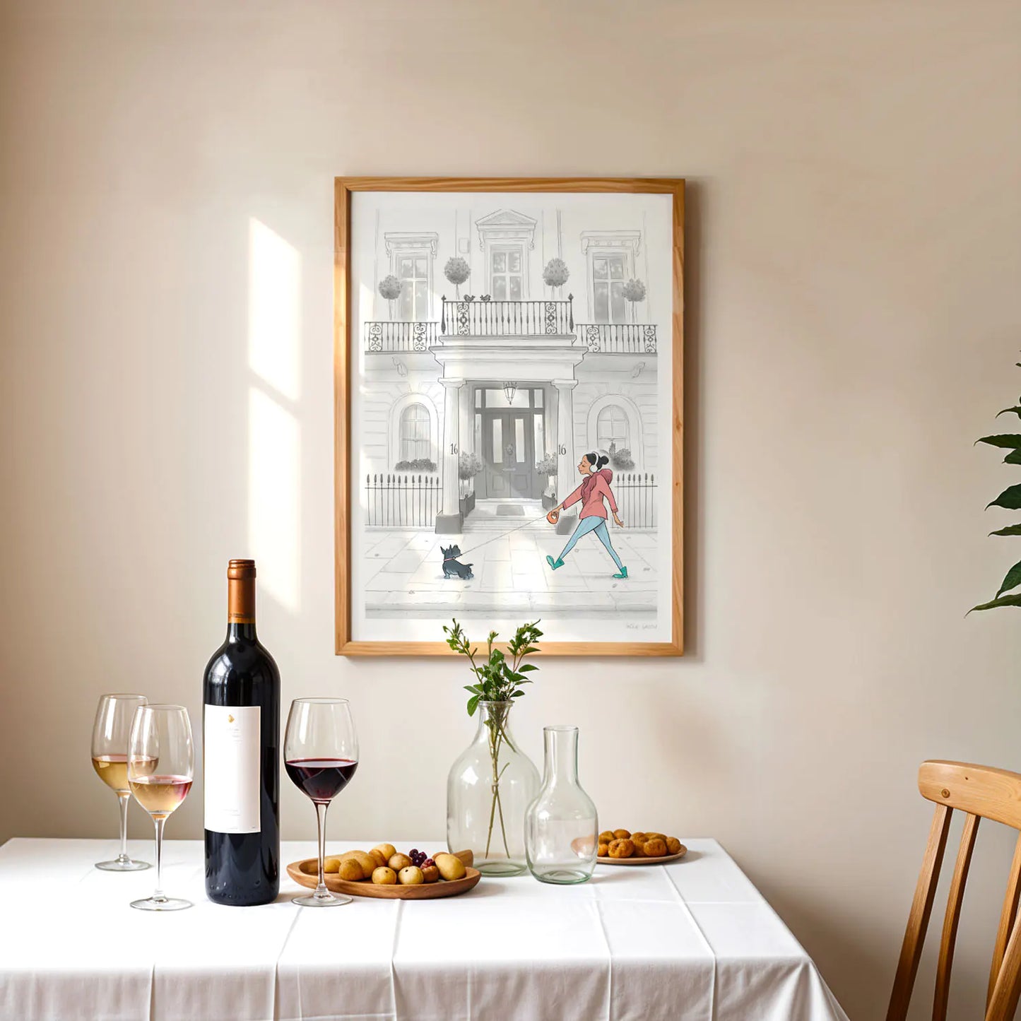 Framed print of a painting of a lady and her dog strolling past a white house in London's Kensington framed above a table with wine