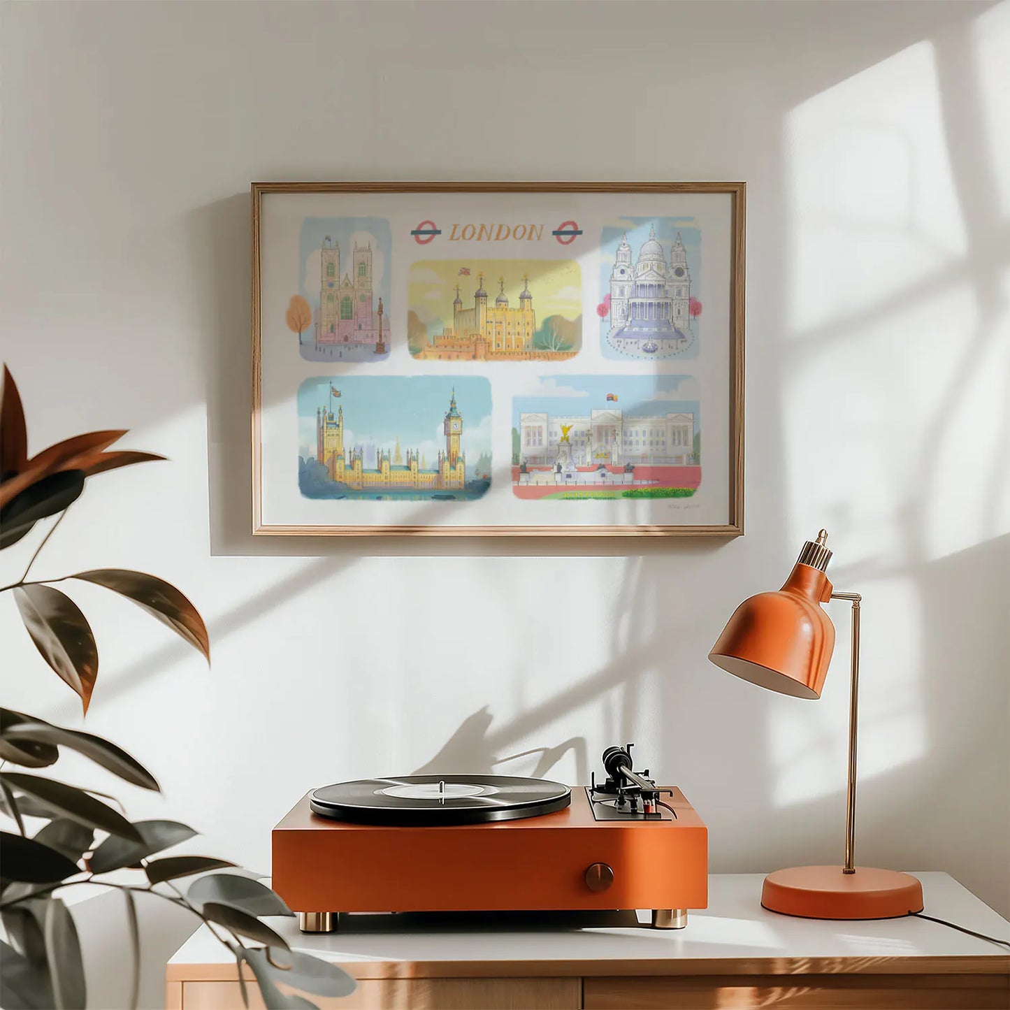A framed art print of London's landmarks including, Westminster Abbey, The Tower of London, St Paul's Cathedral, Palace of Westminster and Buckingham Palace on a wall with a record player and lamp