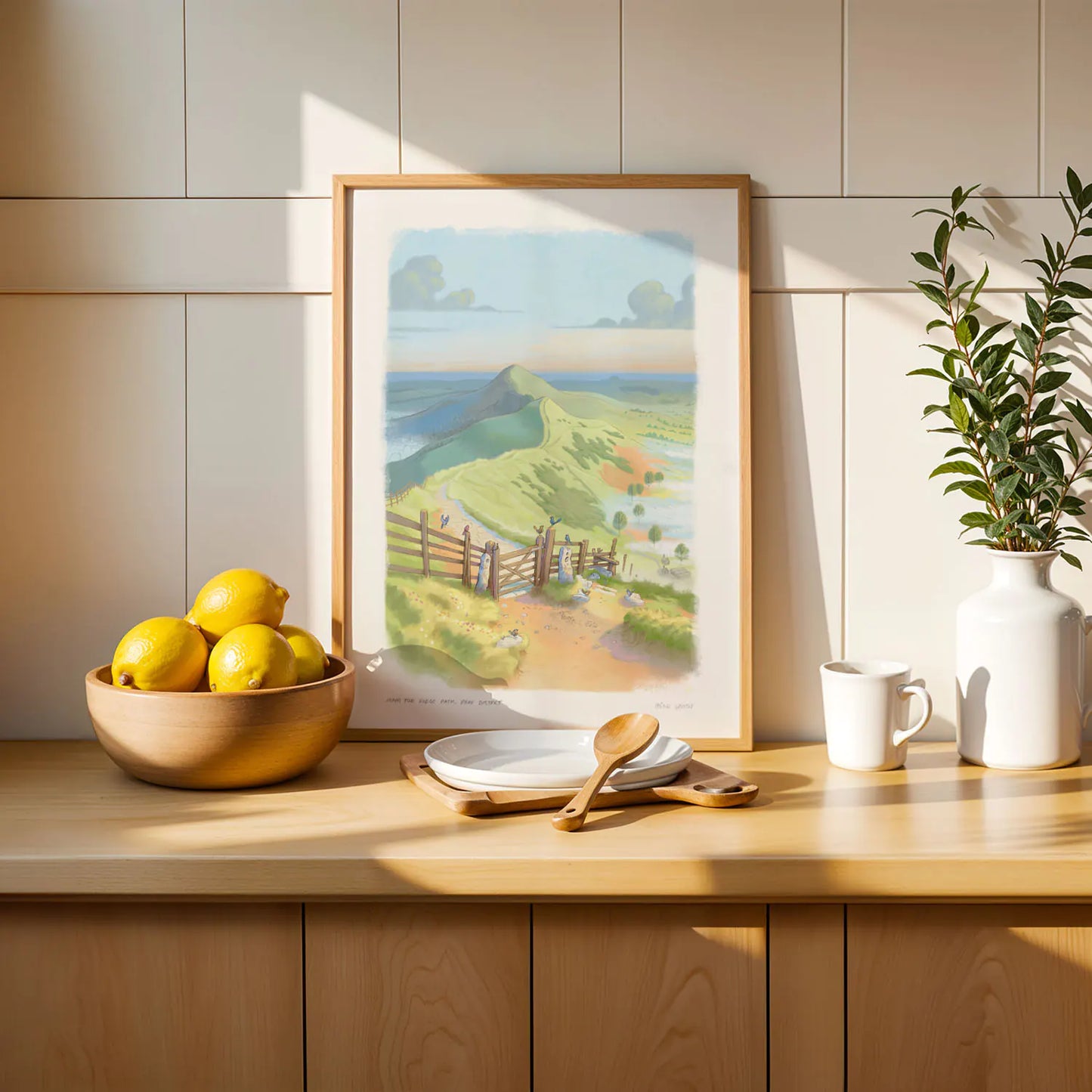 Framed art print of a painting of the Mam Tor Ridge Path in the Peak District in England next to fruit and spoon