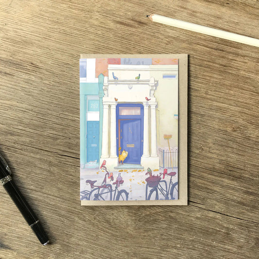 A greetings card with Notting Hill's Blue door from the film with a cat and birds in London on a wooden table