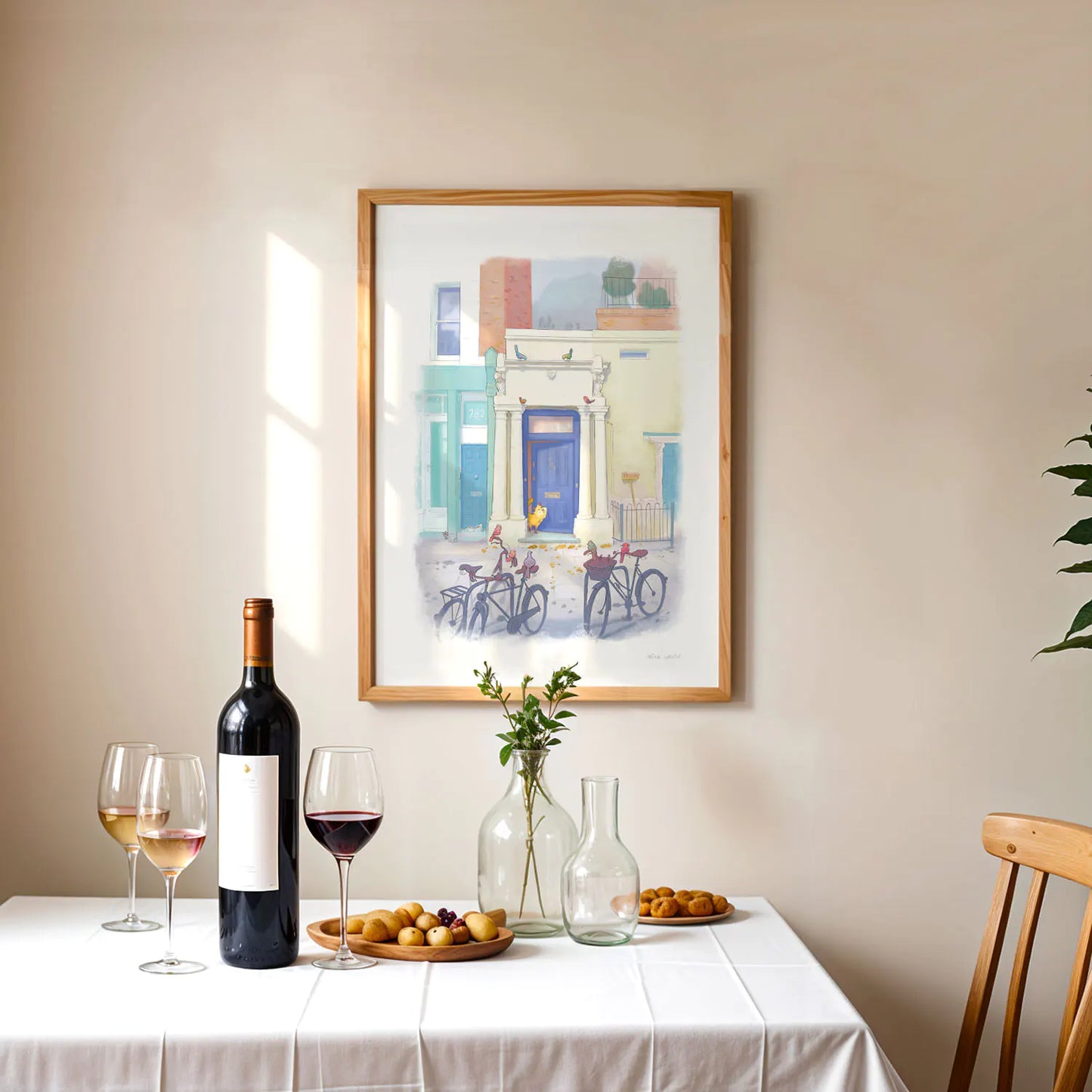 Framed wall art print of a painting of the blue door in London's Notting Hill with a cat watched by a few local birds on bicycles above a table with wine and food