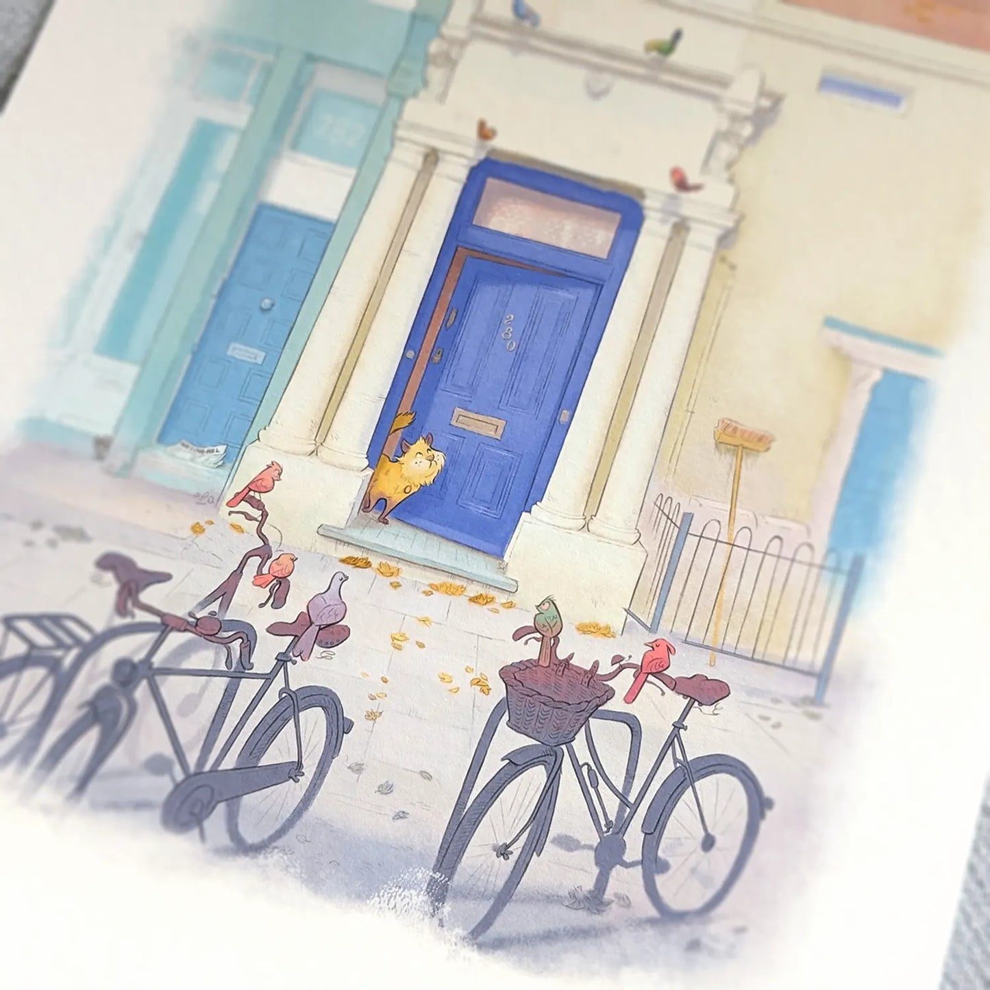 Photo of a wall art print of a painting of the blue door in London's Notting Hill with a cat watched by a few local birds on bicycles