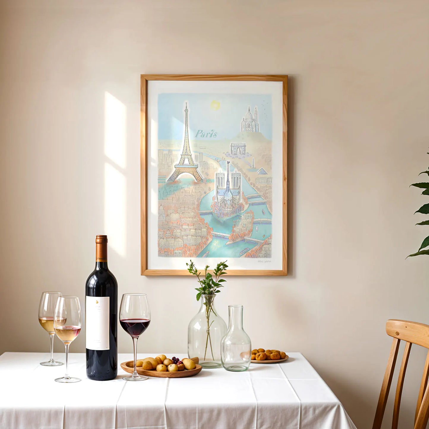 Framed print of an illustration of the Paris skyline and its landmarks above a table with wine and fruit