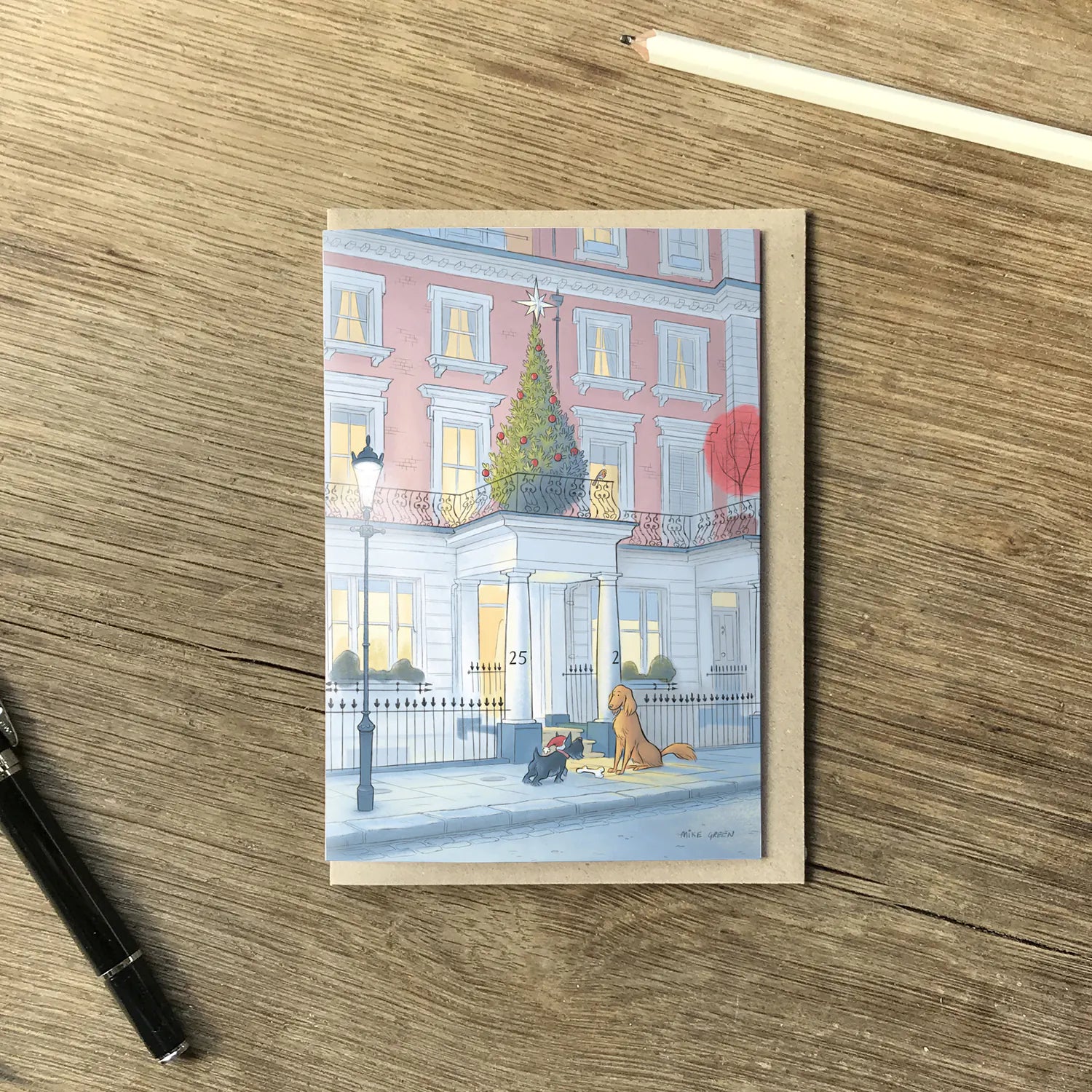 Christmas card with two dogs at Christmas time outside a house on a London street at night on a wooden surface with a pen and pencil