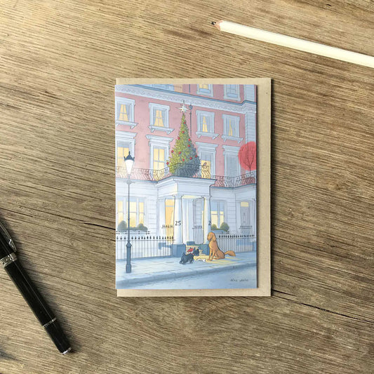 Christmas card with two dogs at Christmas time outside a house on a London street at night on a wooden surface with a pen and pencil
