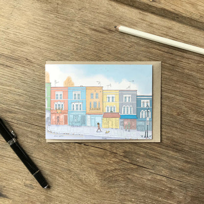Colourful greetings card of Portobello road shops in London's Notting Hill with an envelope and pencil on a wooden surface