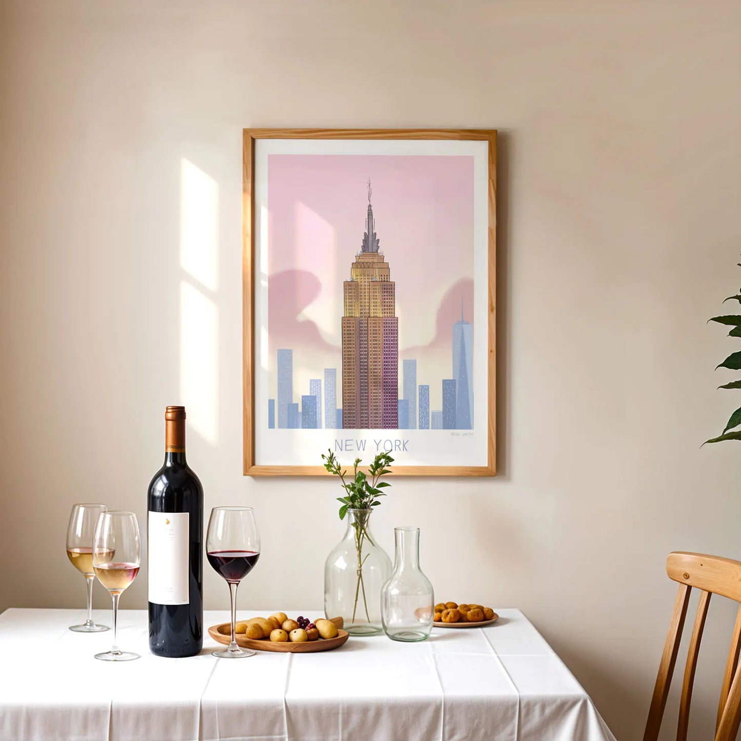 Framed art print of New York's Empire State Building landmark above table with wine