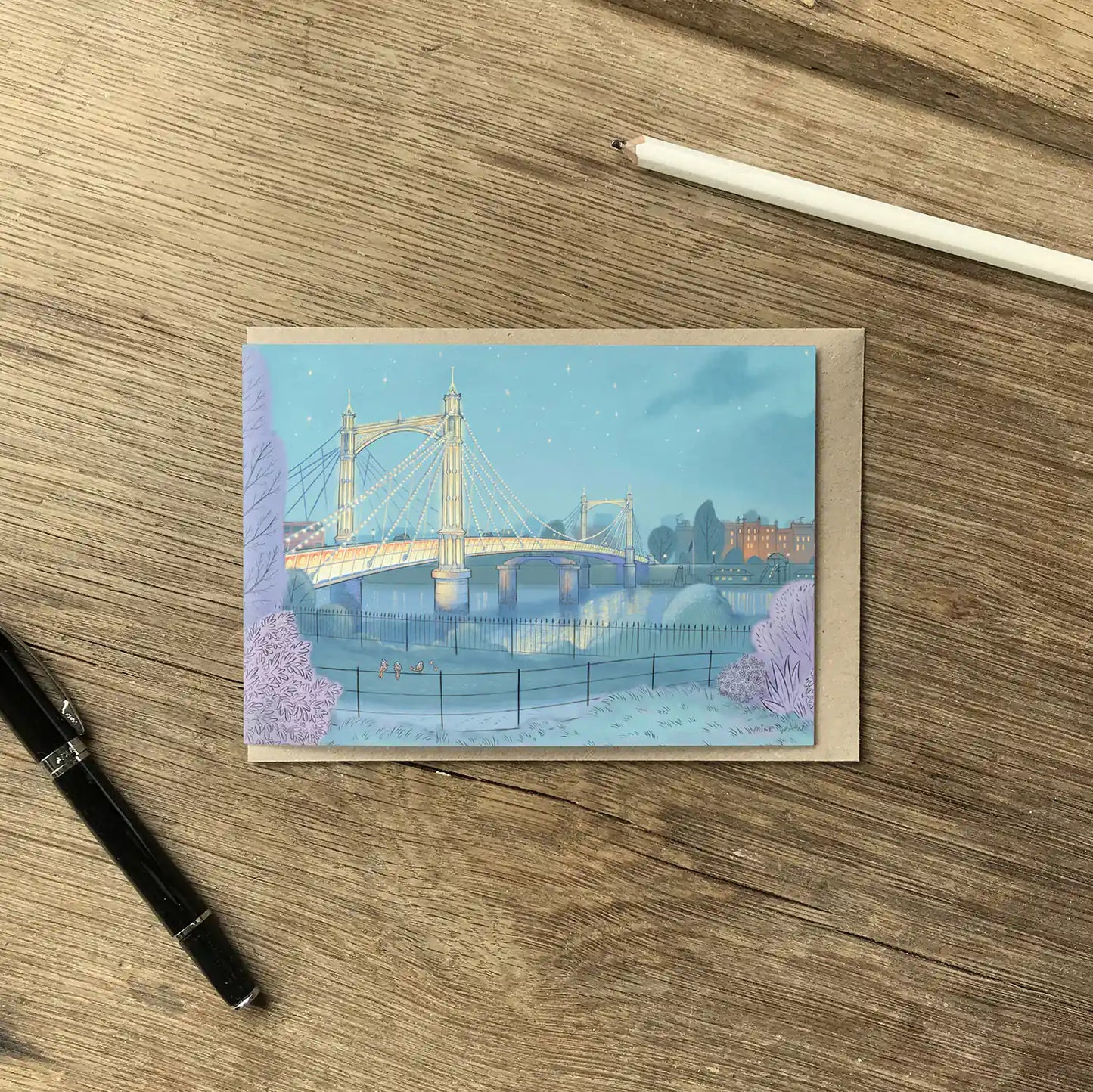 Greetings card of Albert Bridge on the Thames London painted by Mike Green Illustration on a wooden table