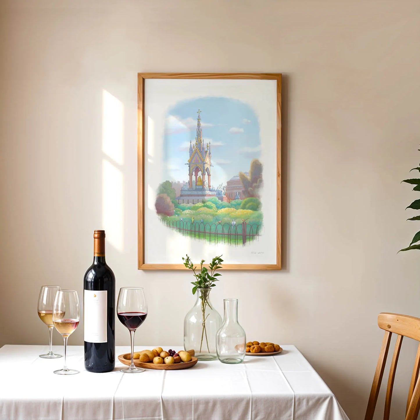 Framed wall art print of a painting of the Albert Memorial in London Hyde Park hanging above a table with wine and fruit
