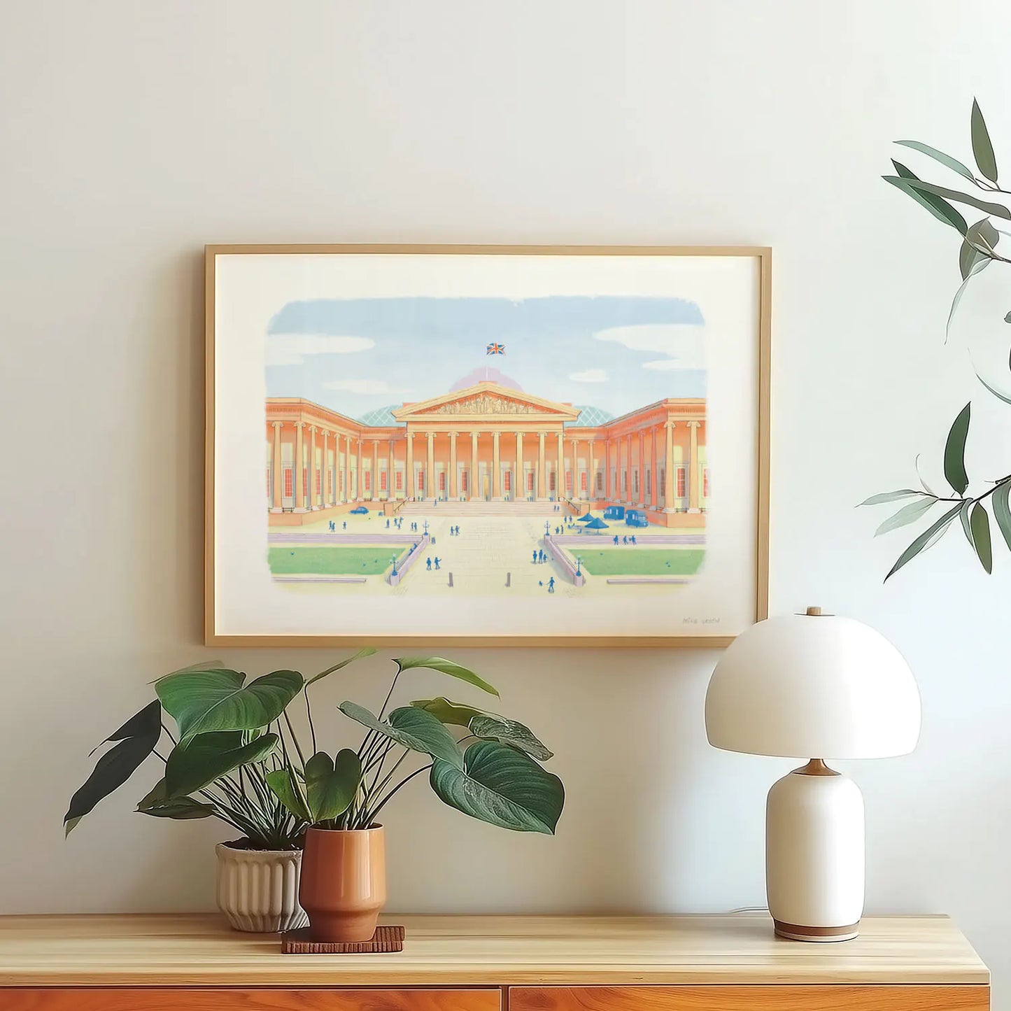 A framed wall art print of London's the British Museum hanging on a wall with a plant and lamp
