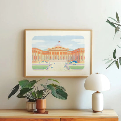 A framed wall art print of London's the British Museum hanging on a wall with a plant and lamp