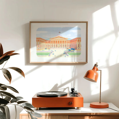 A framed wall art print of The British Museum in London's Bloomsbury hanging on a wall with a record player and lamp