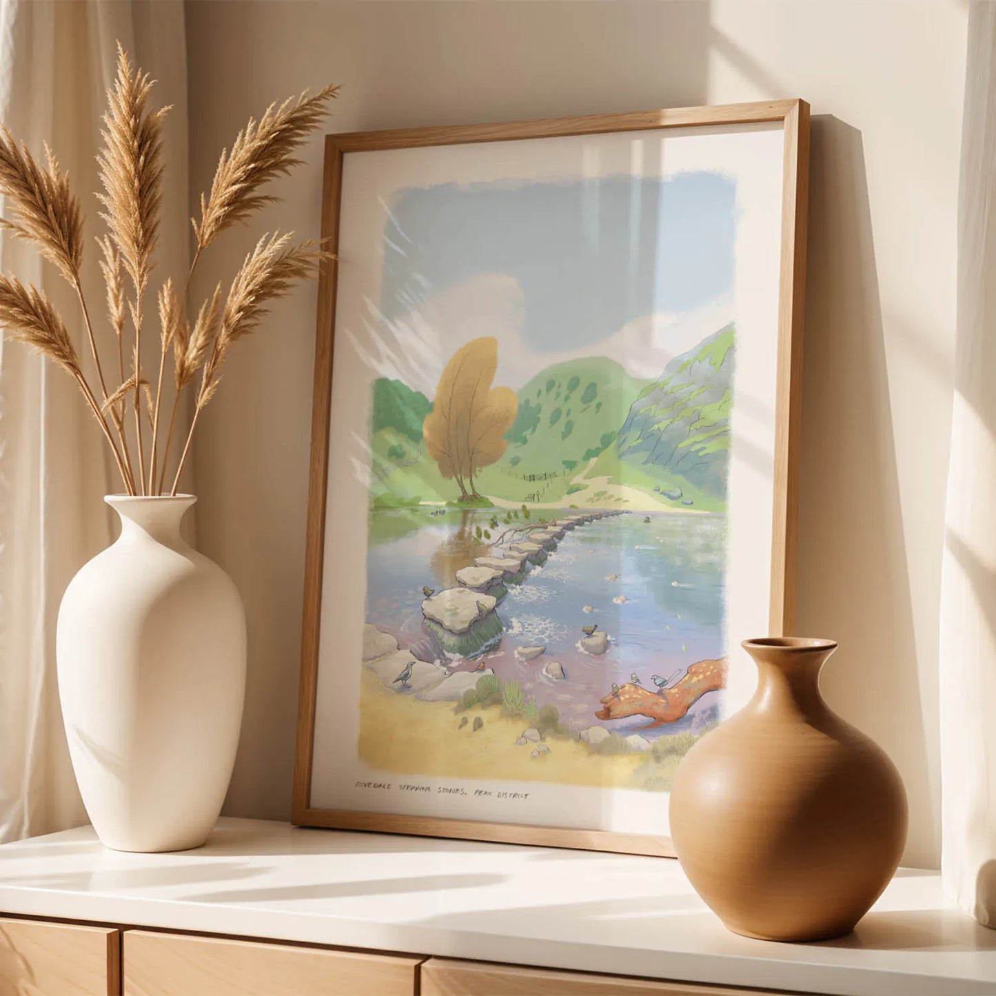 Framed wall art print of a painting of the stepping stones in Dovedale in the Peak District national park on a shelf with vases