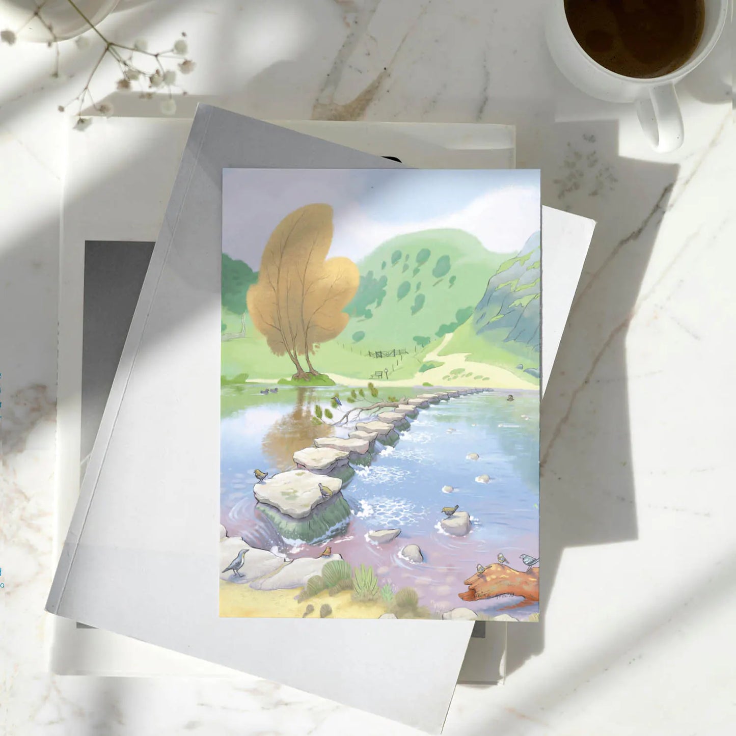Greetings card with a painting of Dovedale Stepping Stones in the Peak District on a pile of books