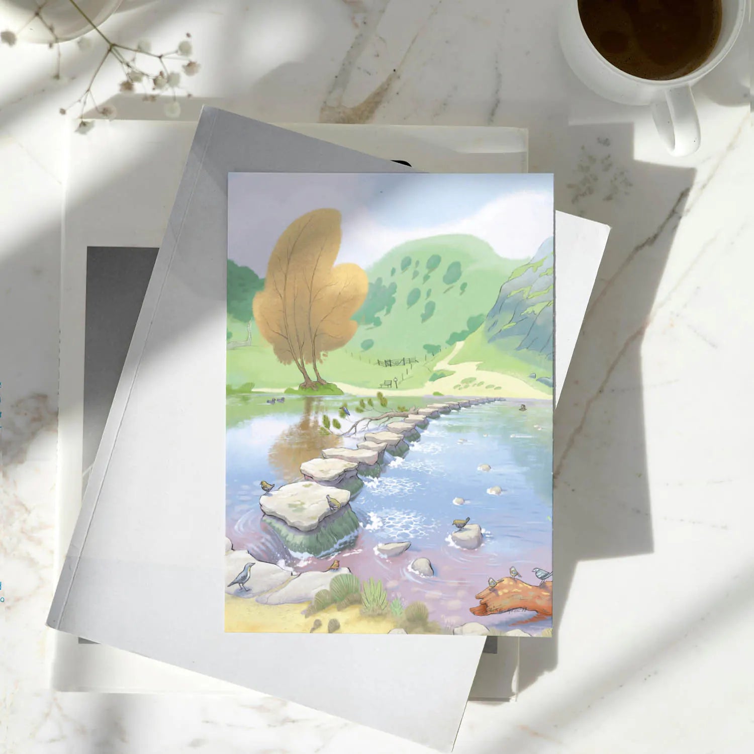 Greetings card with a painting of Dovedale Stepping Stones in the Peak District on a pile of books