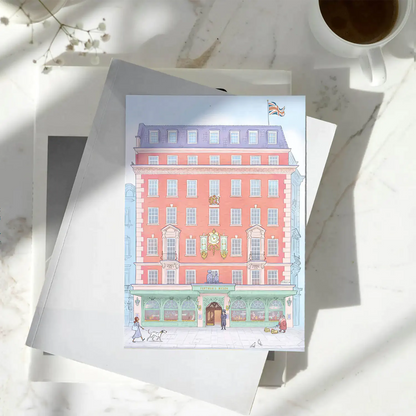 London's Fortnum & Mason store building illustrated on a greeting card resting on a pile of books on a marble surface