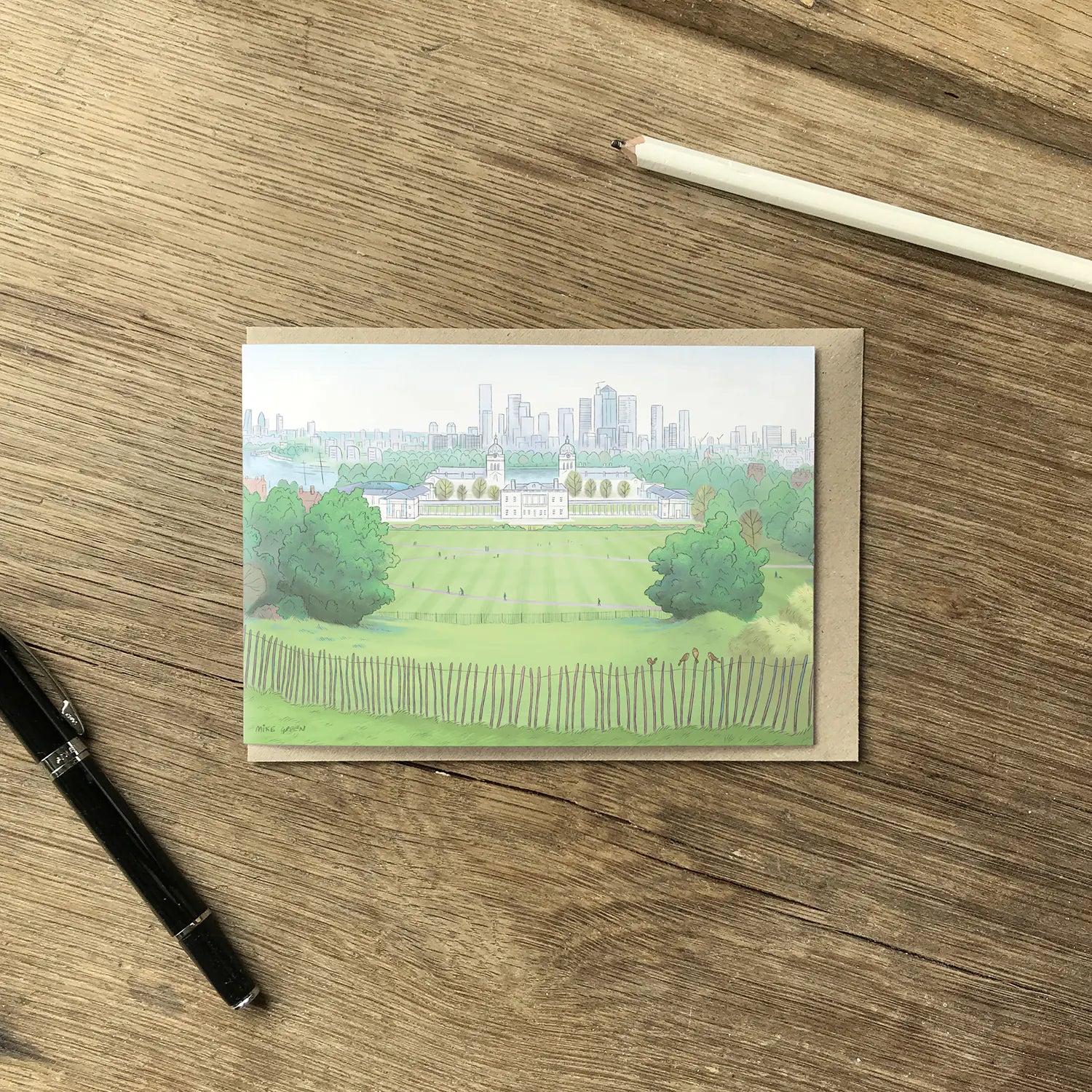 View from London's Greenwich Park  illustrated on a greeting card with an envelope and pencil on a wooden surface