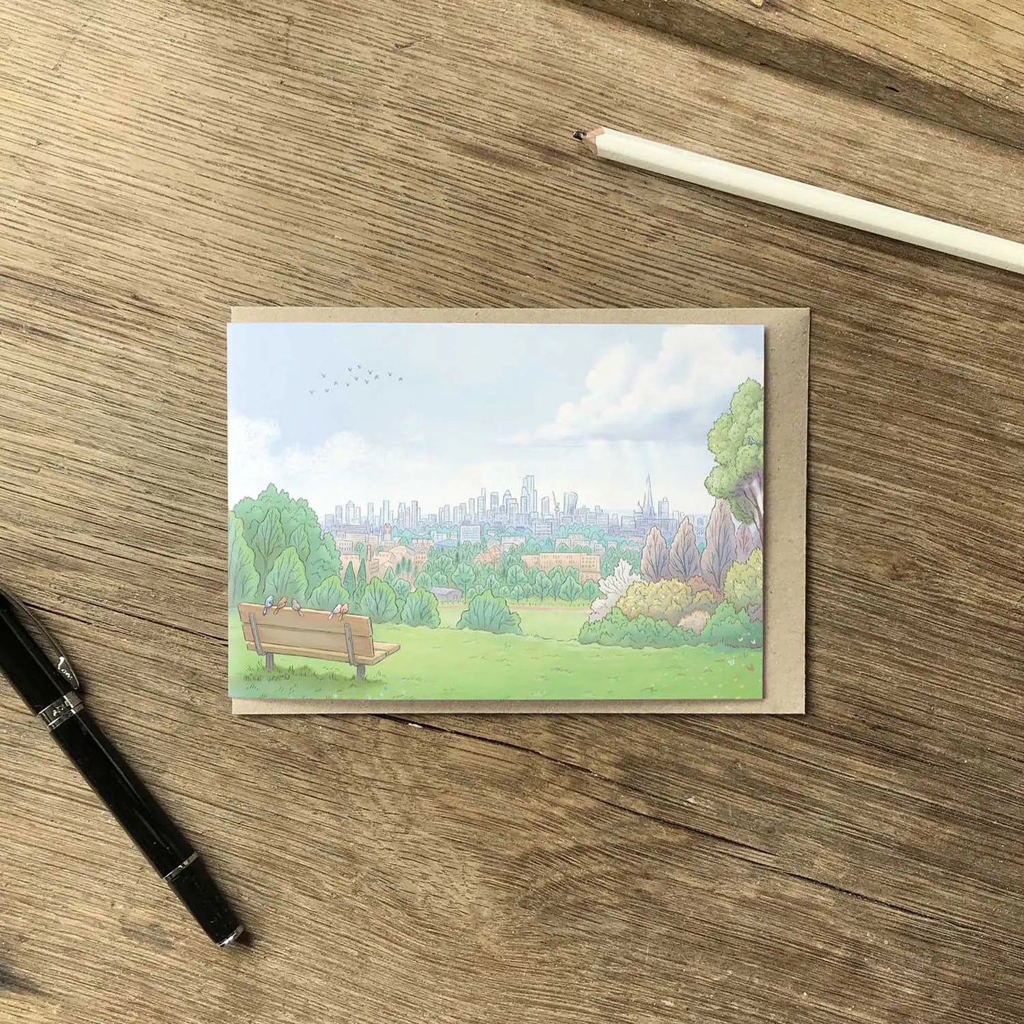 Greetings card with painting of the view from London's Parliament Hill in Hampstead Heath with a pencil on a wooden surface