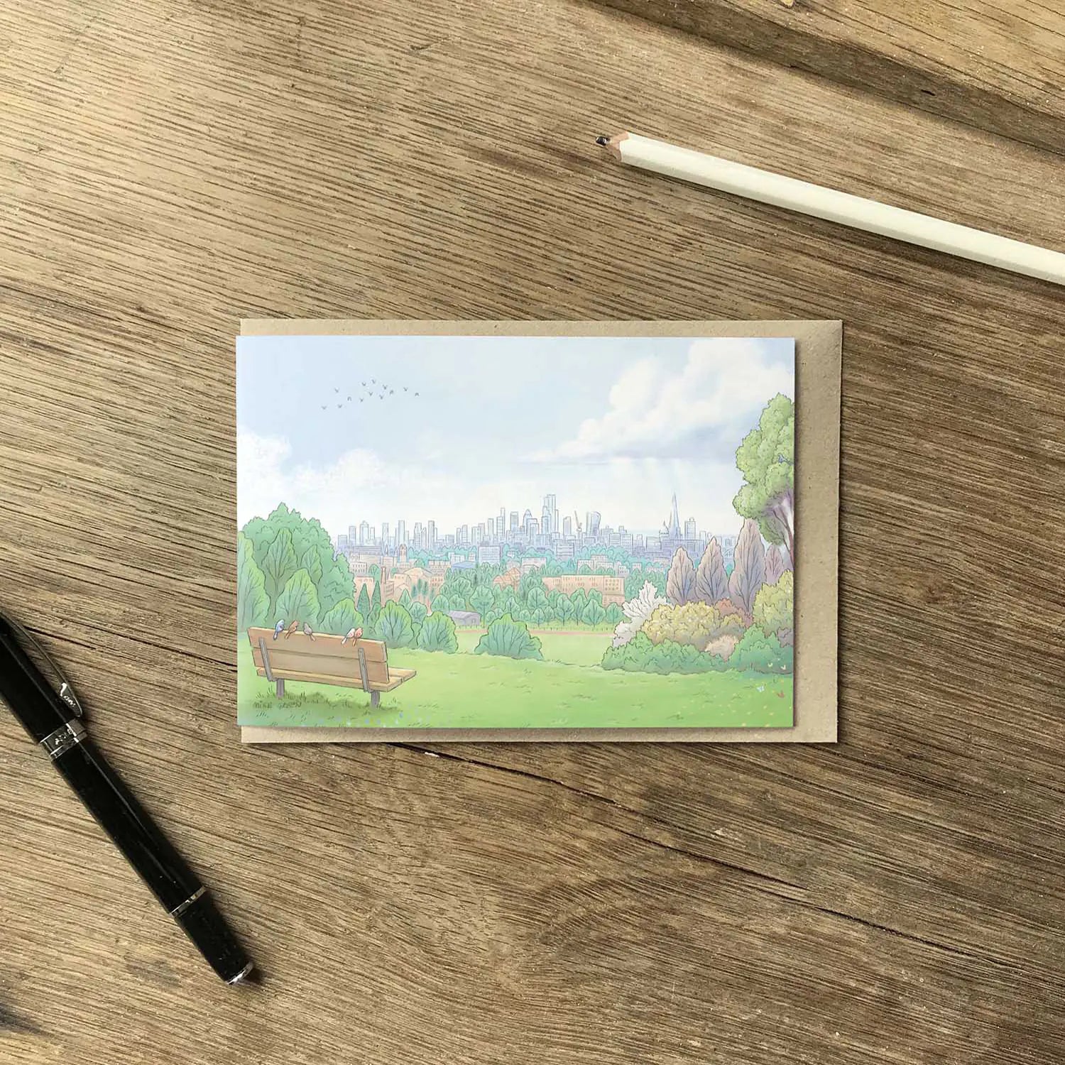 Greetings card with painting of the view from London's Parliament Hill in Hampstead Heath with a pencil on a wooden surface