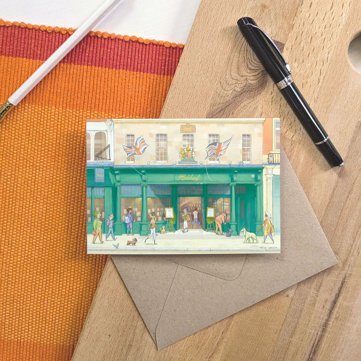 A greetings card featuring a watercolor-style illustration of Hatchards Piccadilly bookshop in London with a kraft envelope behind and pen