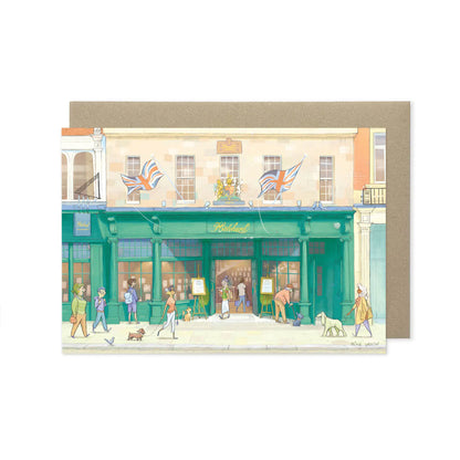 A greetings card featuring a watercolor-style illustration of Hatchards Piccadilly bookshop with people shopping in London with a kraft envelope behind it on a white background.