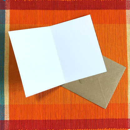 Blank white inside of a greetings card shown with a brown envelope on an orange textured surface