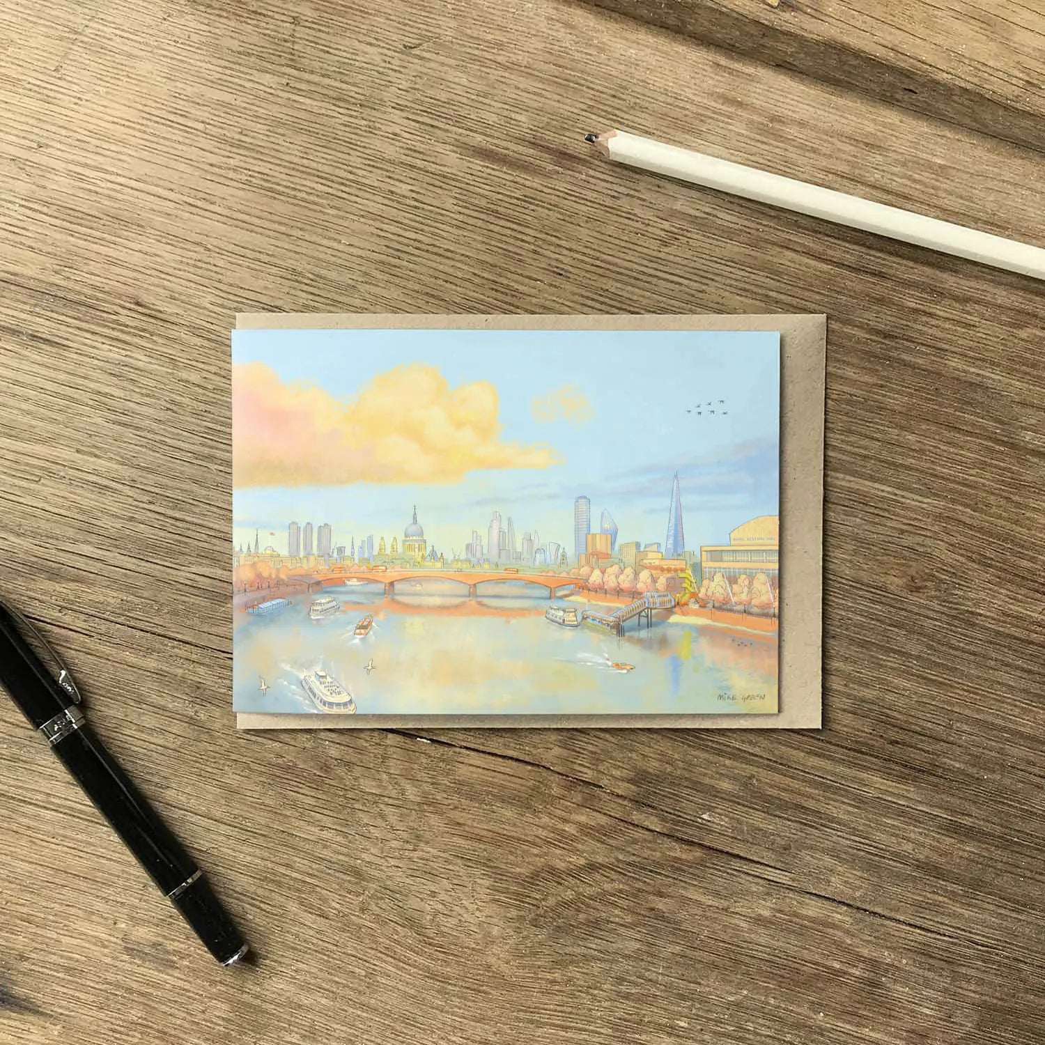 Greetings card with a painting of St Pauls Cathedral, waterloo bridge and the Thames in London in the evening on a wooden surface with a pencil