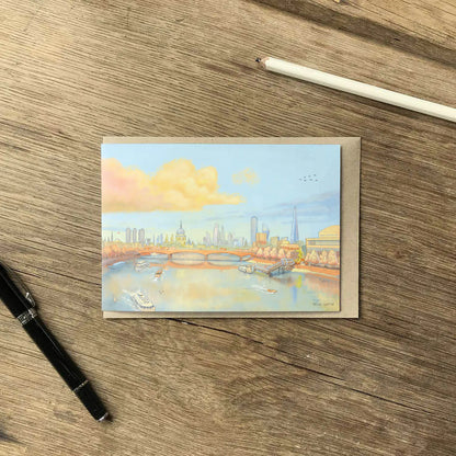 Greetings card with a painting of St Pauls Cathedral, waterloo bridge and the Thames in London in the evening on a wooden surface with a pencil