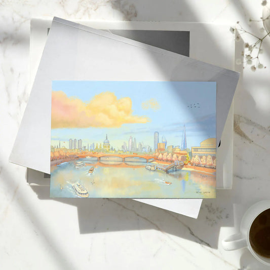 Greetings card with a painting of St Pauls Cathedral, waterloo bridge and the Thames in London in the evening on books on a marble table with a cup of coffee