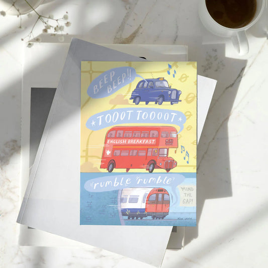 A greetings card with London transport, a red bus, a taxi and a tube train all making sounds resting on a pile of books on a marble surface