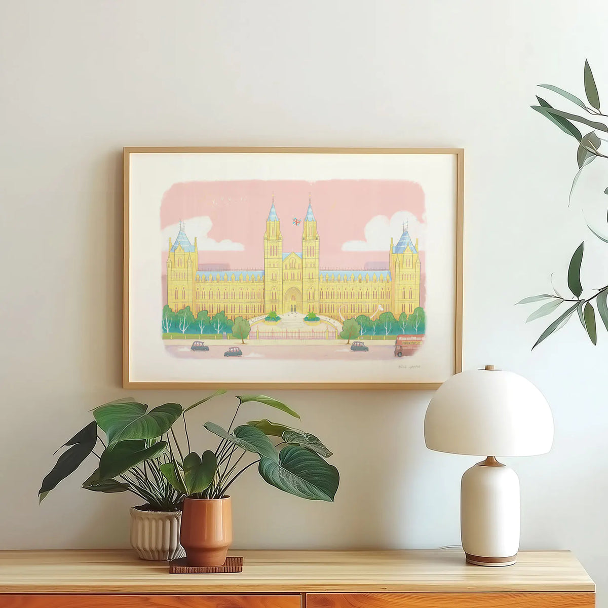 Framed wall art print of the Natural History Museum in London's South Kensington above a table with plants and a lamp