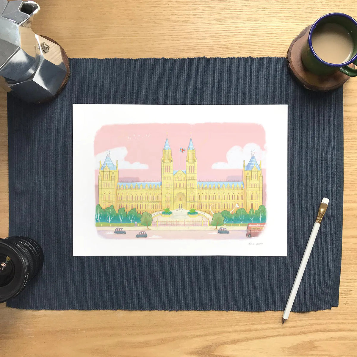 Wall art print of the Natural History Museum in London's South Kensington on a table with a pencil and coffee