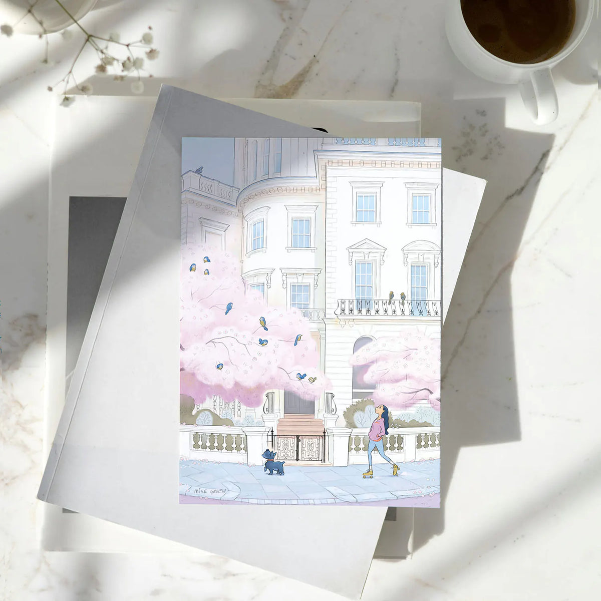A greeting card illustrated with pink blossom, birds and a lady skating with her Scottish terrier dog on a street in London's Notting Hill.