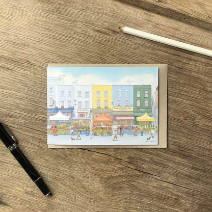 A greetings card of the Portobello Road Market in London's Notting Hill with an envelope and pencil on a wooden surface