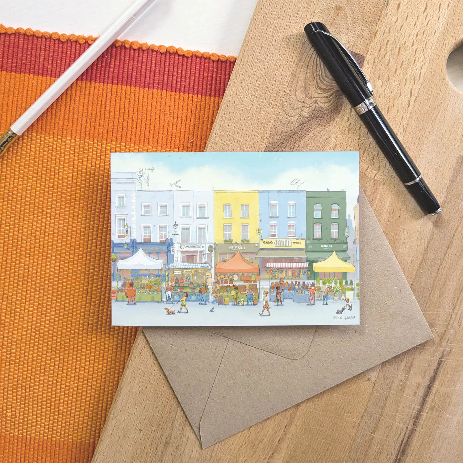 A greetings card of the Portobello Road Market in London's Notting Hill with an envelope and pen on a wooden board