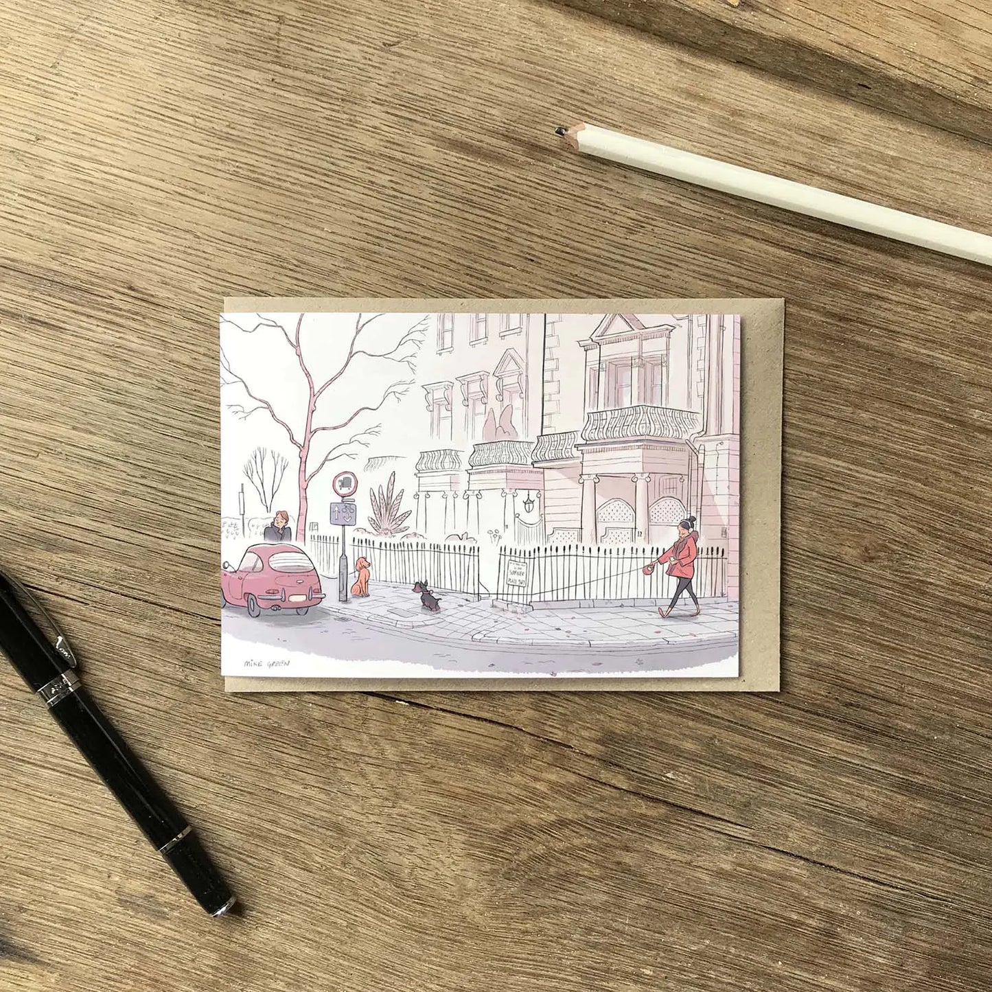 Greetings card with dog walkers on a street in London's Kensington street on a wooden surface with pens