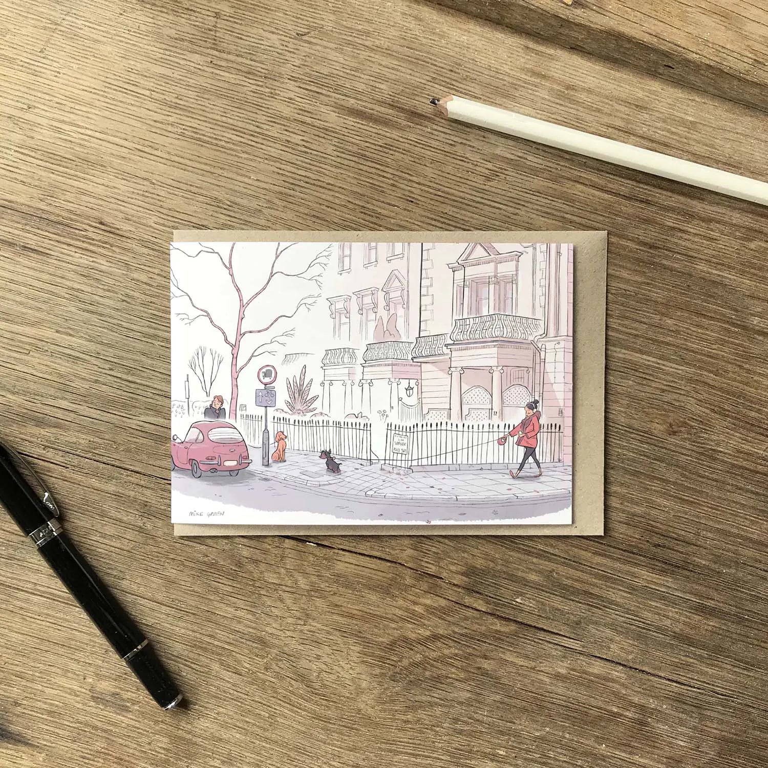 Greetings card with dog walkers on a street in London's Kensington street on a wooden surface with pens