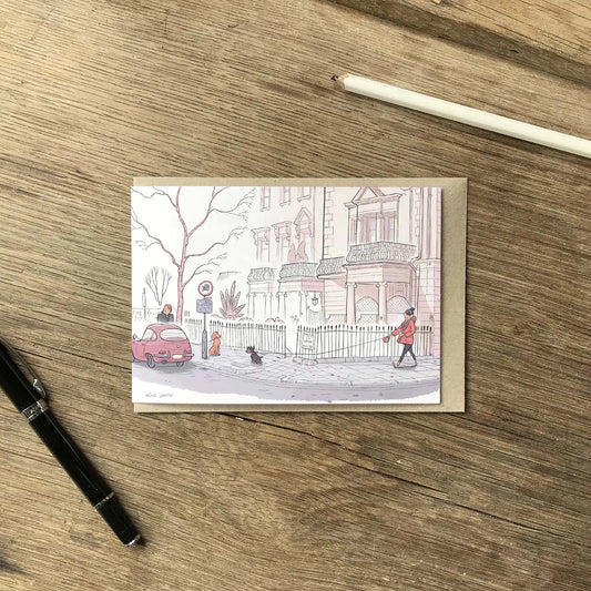 Greetings card with dog walkers on a street in London's Kensington street on a wooden surface with pens