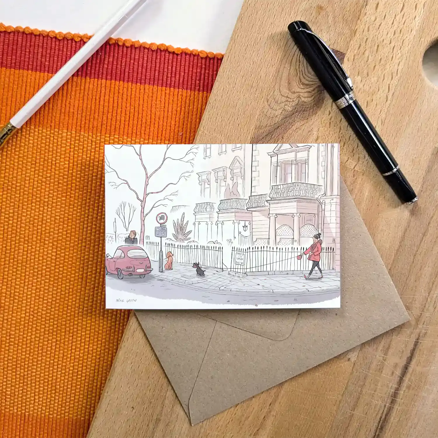Greetings card with dog walkers on a street in London's Kensington street on a wooden surface with pens