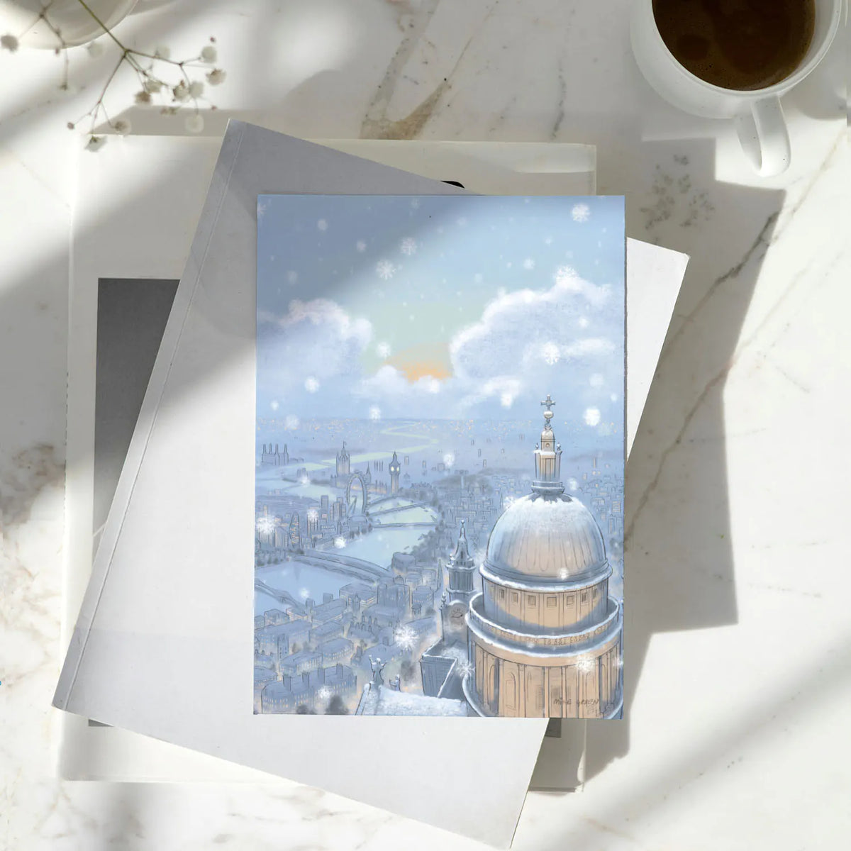Christmas greetings card with London's St Pauls Cathedral in the snow at nighttime shown on a wooden surface with a pencil and pen
