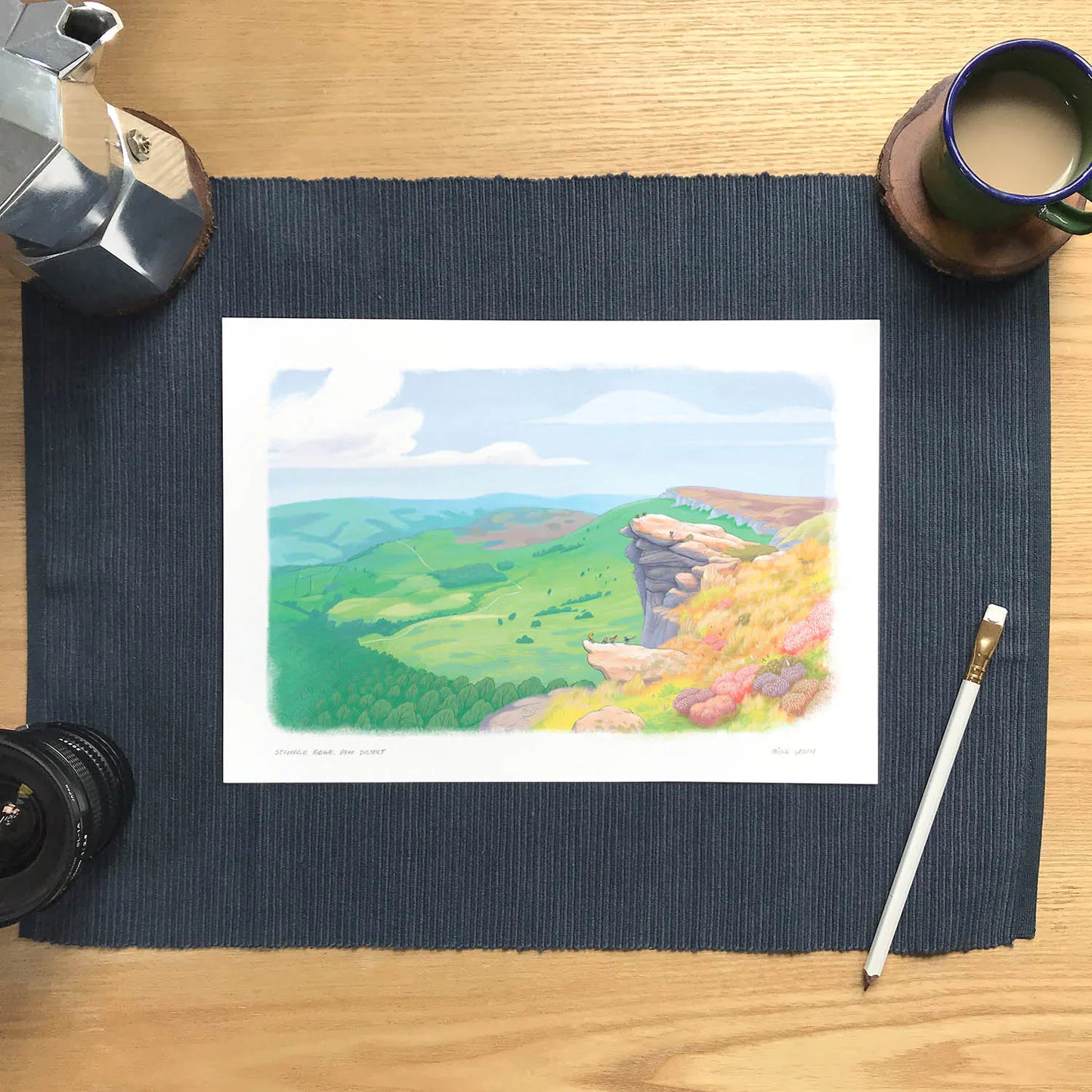 Wall art print of a painting of the view from Stanage Edge in the Peak District National Park in Derbyshire England on a desk with coffee and pencil