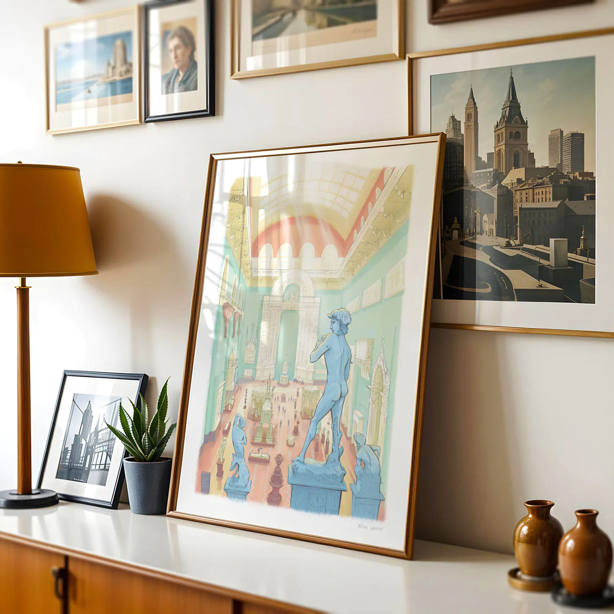 A framed art print of the Victoria and Albert Museum's Weston Cast Court in London's South Kensington on a shelf leaning against a wall with framed photographs.