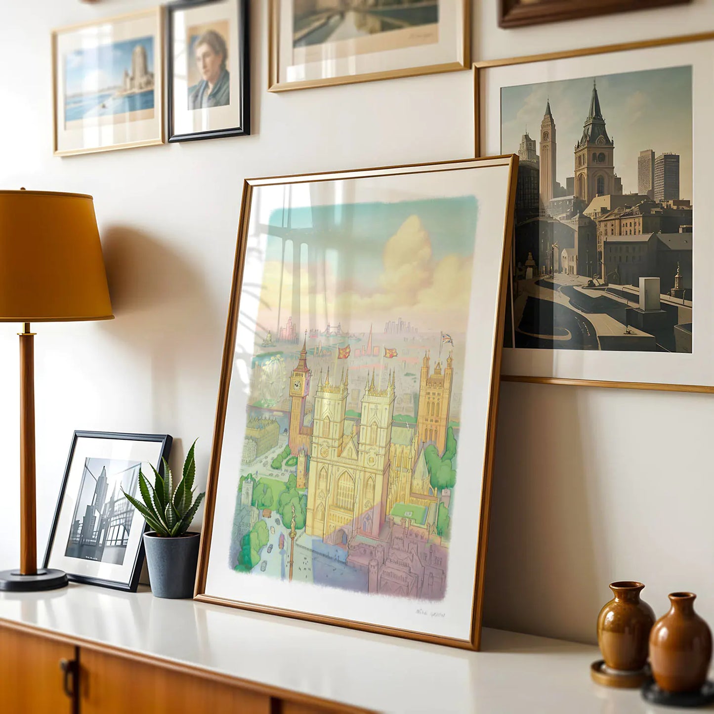 A wall art print of Westminster Abbey in a watercolour illustration style with big ben and the London Eye also shown framed in a room with a lamp and other framed images