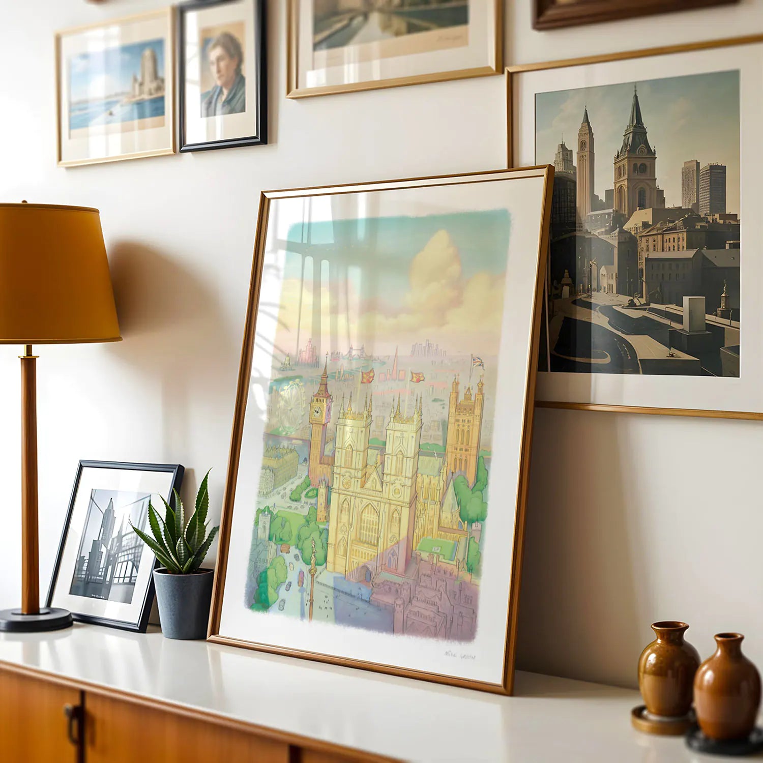 A wall art print of Westminster Abbey in a watercolour illustration style with big ben and the London Eye also shown framed in a room with a lamp and other framed images