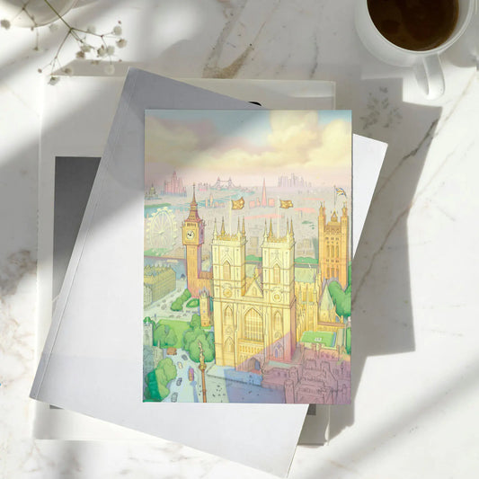 A greetings card featuring a pastel illustration of London landmarks, including Big Ben, Westminster Abbey, and the London Eye, shown with a brown kraft envelope behind it on a pile of books on a marble surface.
